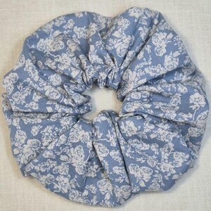 Könnte beinhalten: Ein blauer und weißer Blumenmuster-Haargummi. Der Haargummi ist aus Stoff und hat eine gefaltete Optik.