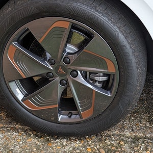 Puede incluir: Primer plano de una llanta de aleación negra y cobre con un diseño de cinco radios. La llanta está montada en un coche blanco.