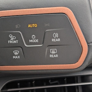 Op de afbeelding: Een close-up van het dashboard van een auto met een paneel met knoppen voor het bedienen van de ruitenwissers en koplampen. De knoppen zijn gelabeld met "Front", "Max", "Mode", "Rear" en "Auto".