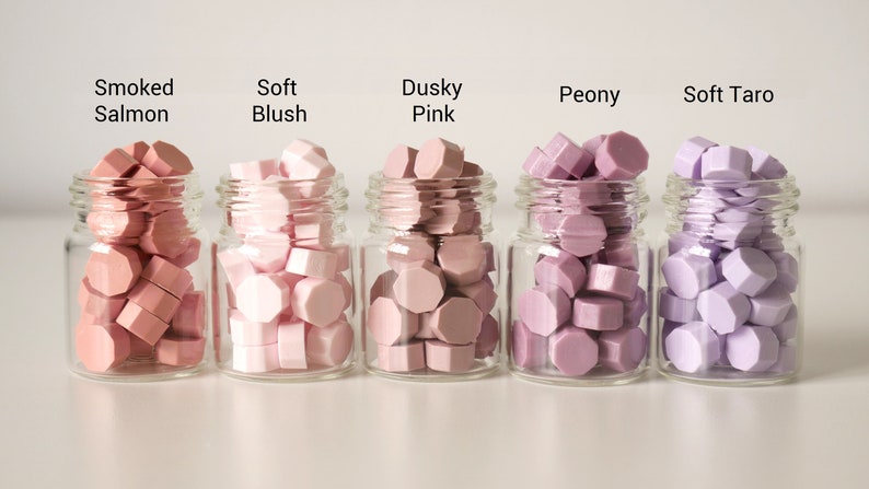 May include: Five small glass jars filled with colorful wax beads. The colors are Smoked Salmon, Soft Blush, Dusky Pink, Peony, and Soft Taro. Each jar has a label with the color name.