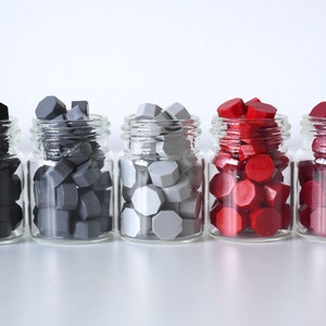 May include: Five small glass jars filled with colorful wax seals. The colors include black, two shades of gray, red, and burgundy. The seals have a geometric shape and are ready for use.