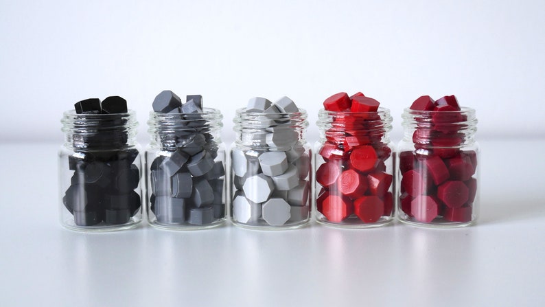 May include: Five small glass jars filled with colorful wax seals. The colors include black, two shades of gray, red, and burgundy. The seals have a geometric shape and are ready for use.