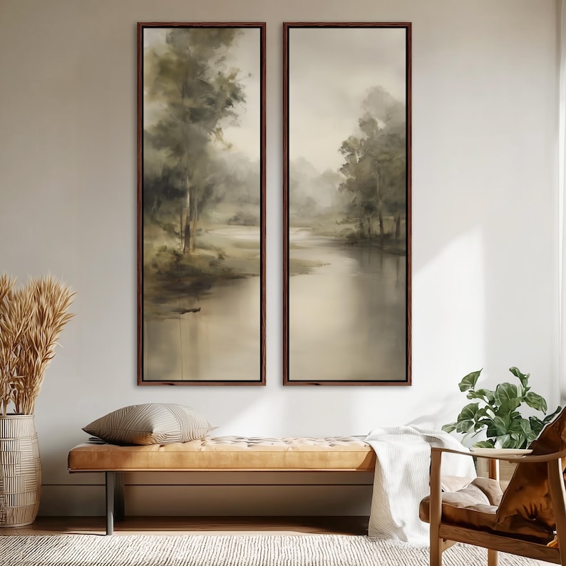 May include: Two tall, vertical rectangular wall art pieces featuring a muted, atmospheric landscape painting of trees along a calm riverbank. The artwork is encased in thin, dark brown wooden frames, displaying soft shades of beige, gray, and olive green.