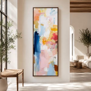May include: Abstract art painting in a vertical rectangular format. The artwork features a blend of colors, including blue, pink, yellow, and orange, with brushstrokes and layered textures. The painting is framed in a dark brown wooden frame.
