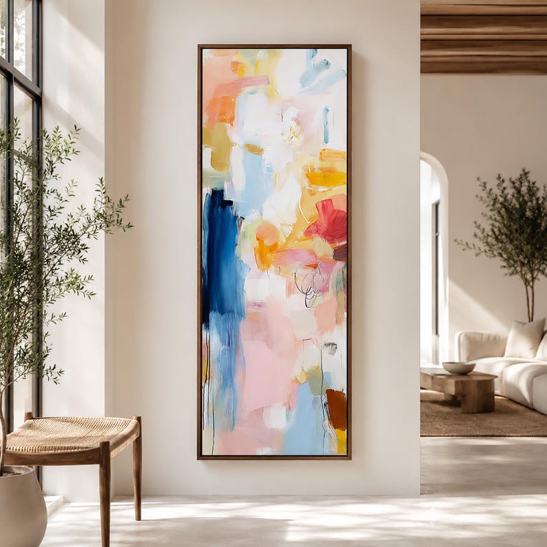 May include: Abstract art painting in a vertical rectangular format. The artwork features a blend of colors, including blue, pink, yellow, and orange, with brushstrokes and layered textures. The painting is framed in a dark brown wooden frame.