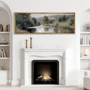 May include: A landscape painting in a gold frame depicts a serene river scene with trees and rolling hills. The artwork hangs above a white marble fireplace with a lit fire, flanked by bookshelves and decorative candles.
