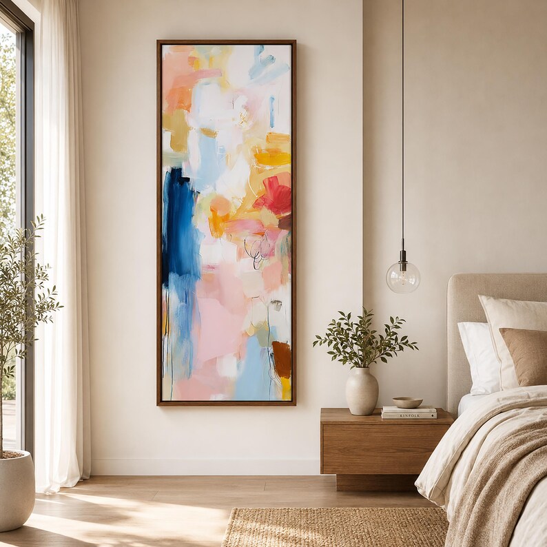 May include: Abstract art painting in a dark wood frame. The artwork features a colorful composition of blue, pink, yellow, and red brushstrokes. The painting is displayed on a neutral-colored wall in a bedroom setting.