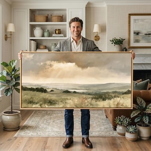 May include: A large rectangular landscape painting in a wooden frame featuring a soft-toned scene of rolling hills, grassy fields, and a distant body of water under a cloudy sky with light rays breaking through the clouds in muted earth tones.
