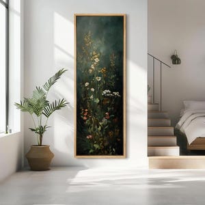 May include: Vertical framed artwork featuring a dark, moody background with a cluster of wildflowers in shades of white, yellow, and pink. The artwork is encased in a light-colored wooden frame, adding a touch of warmth to the piece. The painting evokes a sense of nature and tranquility.