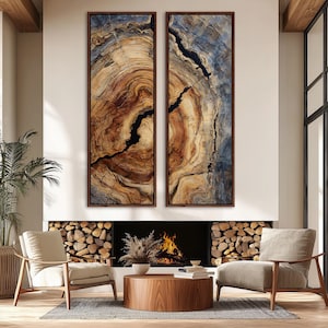 May include: Two framed abstract art pieces depicting cross-sections of wood, showcasing concentric rings in shades of brown, tan, and blue. The artwork is displayed above a fireplace with a burning fire, flanked by chairs and a wooden coffee table.
