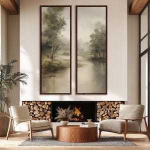 May include: Two tall, vertical rectangular wall art pieces featuring a muted, atmospheric landscape painting of trees and a calm river in shades of beige, brown, and soft green, each enclosed in a thin, dark brown wooden frame.