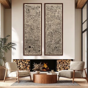 May include: Two framed abstract art pieces with dark brown frames hang above a fireplace. The artwork features a complex pattern of black lines and shapes on a cream background. The room includes a wooden coffee table, chairs, and a fireplace with burning logs.