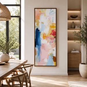 May include: Abstract art painting in a vertical rectangular format. The artwork features a blend of colors, including blue, pink, yellow, and white, with brushstrokes and layered textures. The painting is framed in a dark brown wooden frame.
