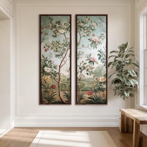 May include: Two framed botanical art prints. Each features a tree with white and pink flowers, set against a light blue background. The artwork includes green foliage and colorful flowers, framed in dark brown.