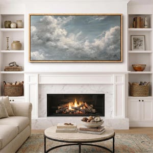 May include: A living room with a fireplace and a large painting of clouds. The painting is framed in gold and hangs above the fireplace. The fireplace has a marble surround and a fire burning inside. There are built-in shelves on either side of the fireplace.