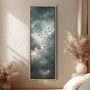 May include: A framed vertical canvas print featuring a dramatic sky filled with dark, ominous clouds. Silhouetted birds are in flight, adding a sense of movement. The artwork is encased in a natural wood frame, creating a striking contrast.