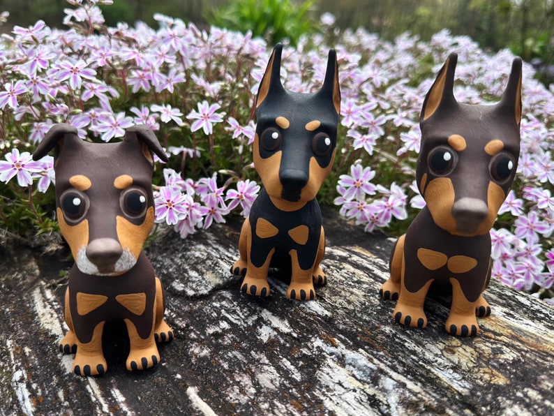 May include: Three small brown and tan dog figurines with black eyes and white noses. The figurines are sitting on a wooden surface.