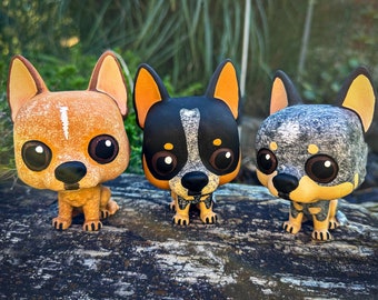 May include: Three small figurines of Australian Shepherd dogs, each with a different colored coat. The first dog is orange and white, the second is black and white, and the third is gray and white.