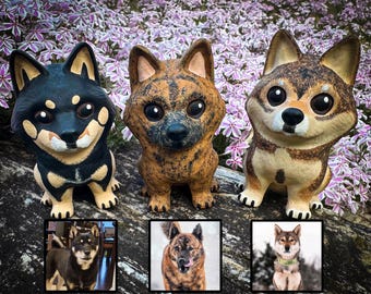 May include: Three hand-painted dog figurines, each with a different breed and color pattern. The figurines are sitting on a wooden surface with pink flowers in the background.