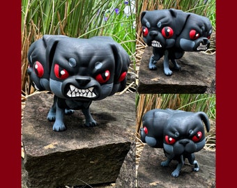 May include: A black three-headed pug figurine with red eyes. Each head has a different expression. The figurine is standing on a gray rock.