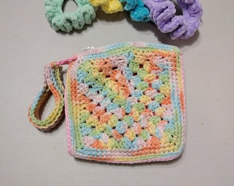 May include: A small crocheted bag with a zipper closure and a colorful granny square design. The bag has a strap and is made with a variety of pastel colors, including pink, blue, green, and yellow.