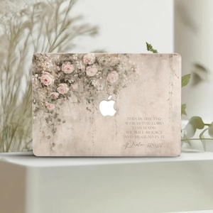 Puede incluir: Una funda para portátil con un diseño floral de rosas rosas y flores blancas. La funda tiene un fondo beige claro con el logotipo de Apple visible. El texto en la funda dice: "Este es el día que hizo el Señor; regocijémonos y alegrémonos en él."