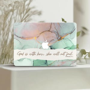 Puede incluir: Una piel para portátil con un diseño de mármol verde, rosa y dorado. La piel tiene el texto "Dios está con ella, ella no fallará. Salmos 46:5" impreso en ella.
