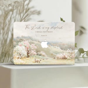 Puede incluir: Una piel para portátil con una pintura de acuarela de una escena pastoral con árboles y ovejas. El texto "The Lord is my shepherd I shall not want Psalm 23" está impreso en la piel.