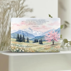 May include: A rectangular print featuring a watercolor landscape of snow-capped mountains, a forest of pine trees, and a blooming pink cherry blossom tree in a meadow. The text reads: SURELY GOODNESS AND MERCY WILL FOLLOW ME ALL THE DAYS OF MY LIFE, AND I WILL DWELL IN THE HOUSE OF THE LORD FOREVER Psalm 23:6.