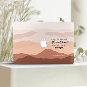 Puede incluir: Una piel para portátil con un diseño de montañas en color melocotón y marrón. El texto "Puedo hacerlo todo por medio de él que me fortalece. Filipenses 4:13" está impreso en la piel.