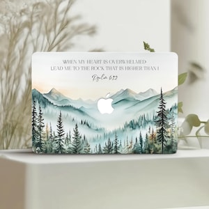 Puede incluir: Funda blanca para portátil con una escena de montaña en acuarela en tonos azules y verdes, con pinos. El texto dice: «CUANDO MI CORAZÓN ESTÁ ABRUMADO: LLÉVAME A LA ROCA QUE ES MÁS ALTA QUE YO Salmo 61:2».
