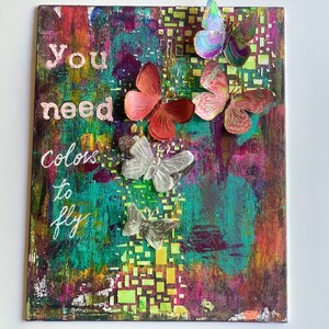 May include: A colorful abstract painting with the text "you need colors to fly" and several paper butterflies in various colors.