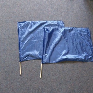 Puede incluir: Dos banderas de tela azul con palos de madera. Las banderas son rectangulares y están hechas de un material sedoso.