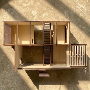 May include: A small wooden doll's house featuring multiple rooms, a staircase, and a balcony. Constructed from light-coloured wood with darker brown accents. The design incorporates open spaces and vertical slat details.