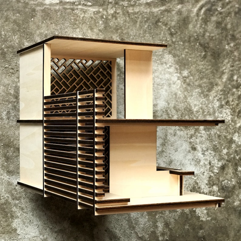 May include: A wooden model of a modern house with a slatted facade and a lattice window. The model is made of light wood and has a simple, geometric design.