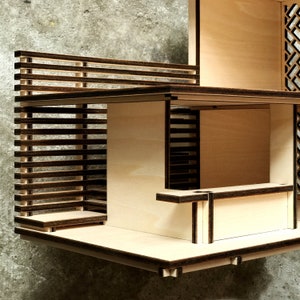 May include: A wooden model of a modern house with a slatted fence and a balcony. The house has a flat roof and a simple design.