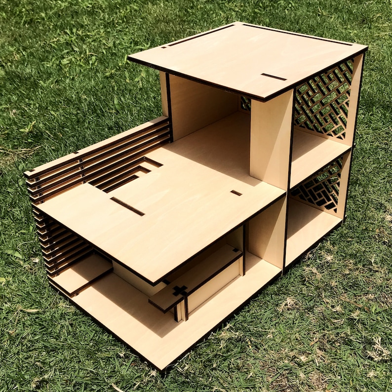May include: A wooden model of a house with a flat roof and a lattice design on the side. The model is made of light brown wood and has a simple, modern design.