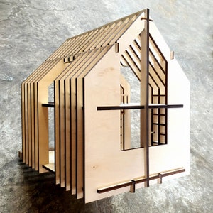 Puede incluir: Un modelo de madera de una casa con un techo a dos aguas y varias ventanas. El modelo est&aacute; hecho de madera contrachapada fina y tiene un acabado de madera natural.