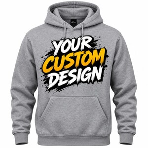 May include: A heather gray hooded sweatshirt featuring a front kangaroo pocket, long sleeves, and a drawstring hood. The center of the chest displays the text "YOUR CUSTOM DESIGN" in a bold, brush-stroke style with white and yellow lettering.