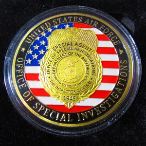 Może przedstawiać: Złota moneta z wzorem amerykańskiej flagi w kolorze czerwonym, białym i niebieskim. Na monecie widnieje tekst "United States Air Force Office of Special Investigations Special Agent" oraz "The Inspector General 1948".