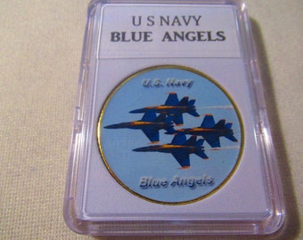 Peut inclure: Une pièce ronde de couleur or avec une image bleue et blanche de trois avions de l'US Navy Blue Angels volant en formation. La pièce porte les inscriptions "U.S. Navy" et "Blue Angels".