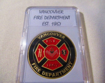 May include: A gold-colored coin with a black and red design. The coin features the words "Vancouver Fire Department Est. 1867" and a stylized fire department logo.