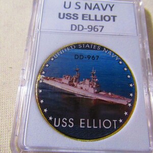 May include: A gold-colored coin with a blue and white image of a ship, the USS Elliot, with the text "United States Navy" and "DD-967" around the edge. The coin also has the text "USS Elliot" at the bottom.