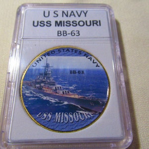 May include: A gold-colored coin with a blue and white image of the USS Missouri battleship. The coin has the text "United States Navy" and "BB-63" on it.