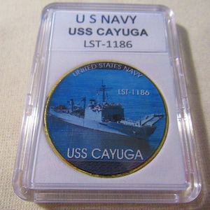 May include: A gold-colored coin with a blue and white image of the USS Cayuga, a ship in the United States Navy. The coin has the text "UNITED STATES NAVY" and "LST-1186" on it.