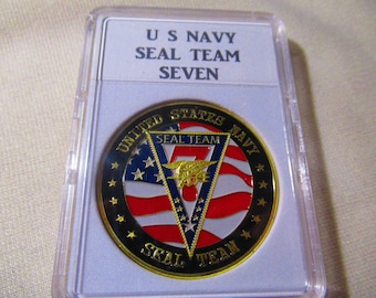 May include: A gold-colored coin with a black border and a red, white, and blue American flag design. The coin features the words "United States Navy" and "SEAL TEAM" in a gold-colored font. The number "7" is visible in the center of the coin.