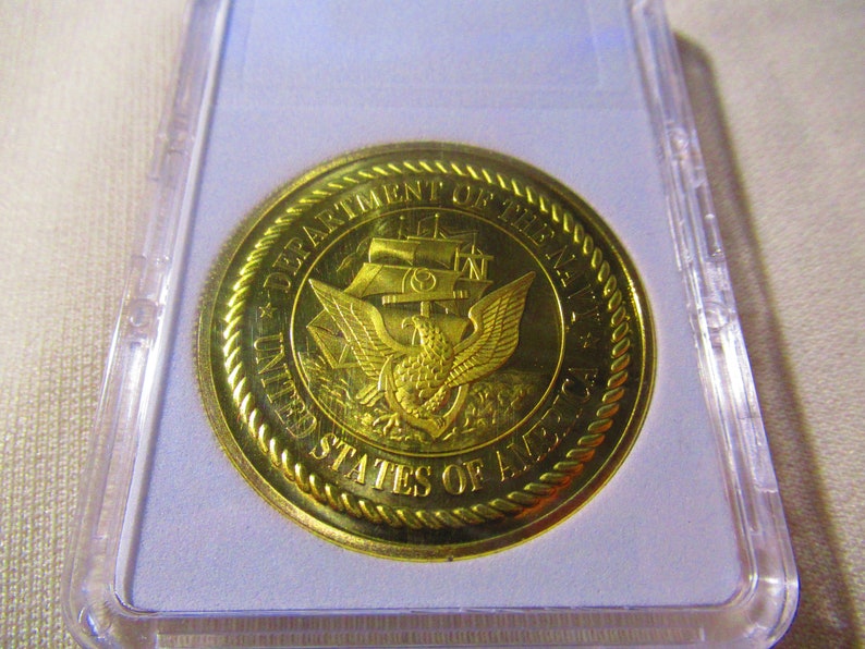 Op de afbeelding: Een gouden munt met de inscriptie "Department of the Navy United States of America" en een adelaar met een anker in zijn klauwen.
