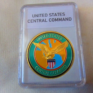 May include: A gold-colored coin with a green, blue, and orange design. The coin features a bald eagle with a shield and the text "UNITED STATES CENTRAL COMMAND".