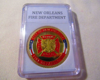 May include: A gold-colored coin with a red and white design. The coin features the words "City of New Orleans" and "Fire Department" around the edge. The center of the coin features a red cross with the words "New Orleans" and "N.O.F.D." inside.