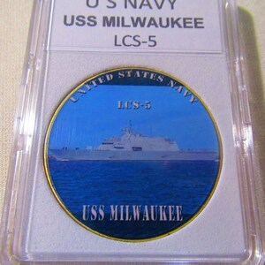Puede incluir: Una moneda de desafío de color dorado con una imagen azul y blanca del USS Milwaukee, un barco de la Armada de los Estados Unidos. La moneda tiene el texto "UNITED STATES NAVY" y "LCS-5" en la parte superior y "USS MILWAUKEE" en la parte inferior.
